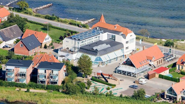 A coastal town with a mix of residential and commercial buildings, including a prominent white building with a red roof and a large glass facade. - 4 Person Holiday Home on a Holiday Park in Hejls (Hejls)