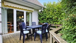 Um deck de madeira com mesa e cadeiras, uma área de varanda coberta e um cercado de madeira.