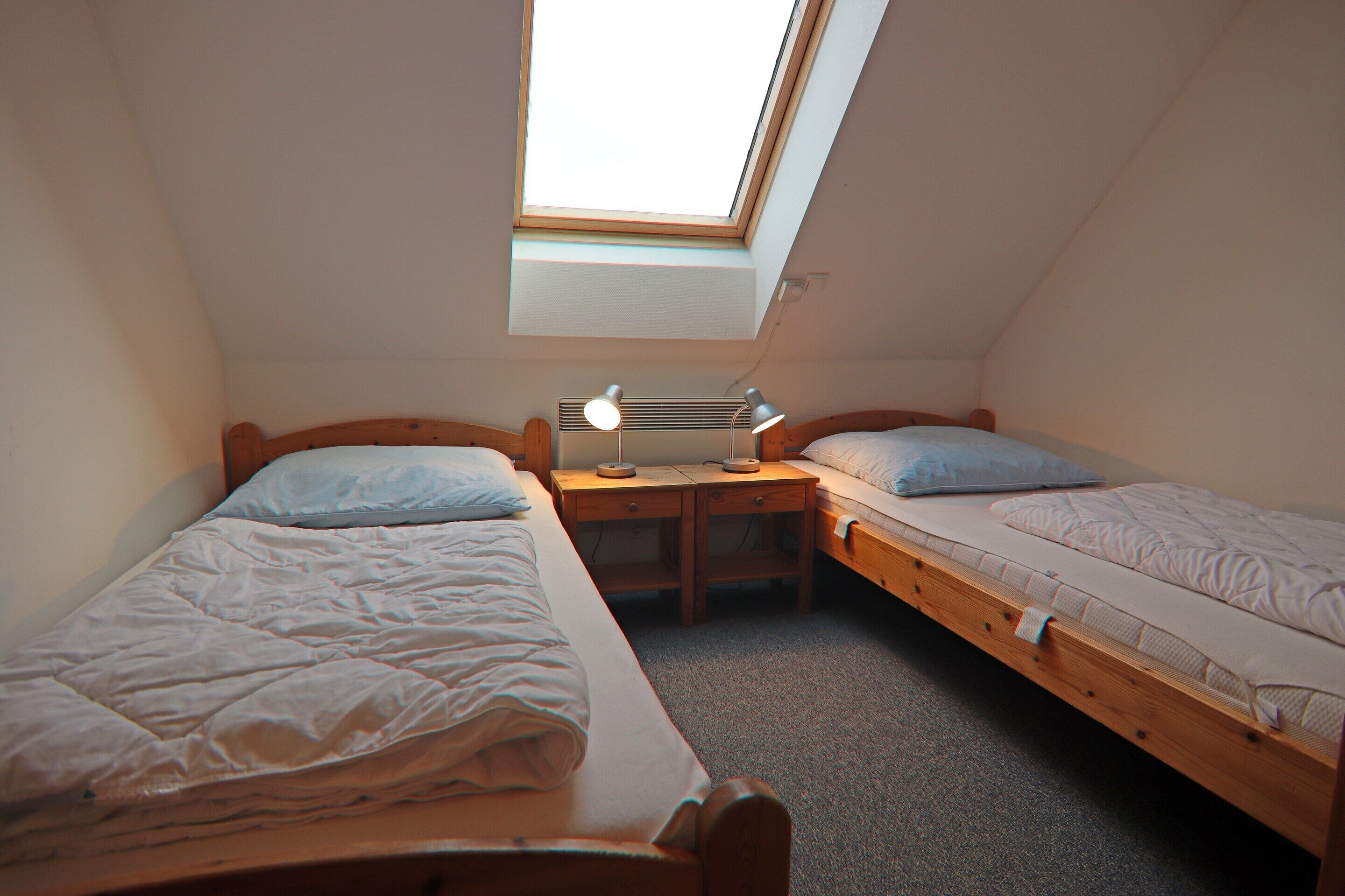 A small, cozy room with two wooden beds, a desk, and a skylight.