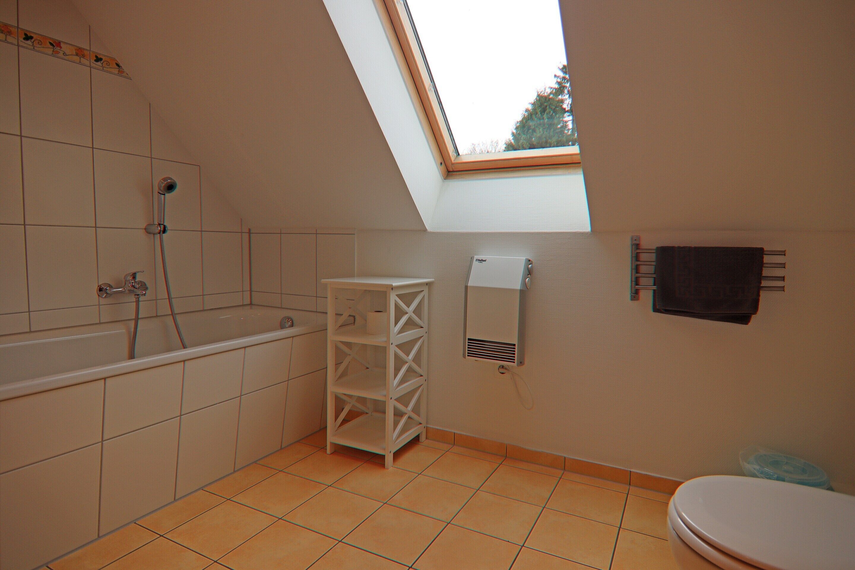 A bathroom with a skylight, a bathtub, a toilet, and a shelf unit.