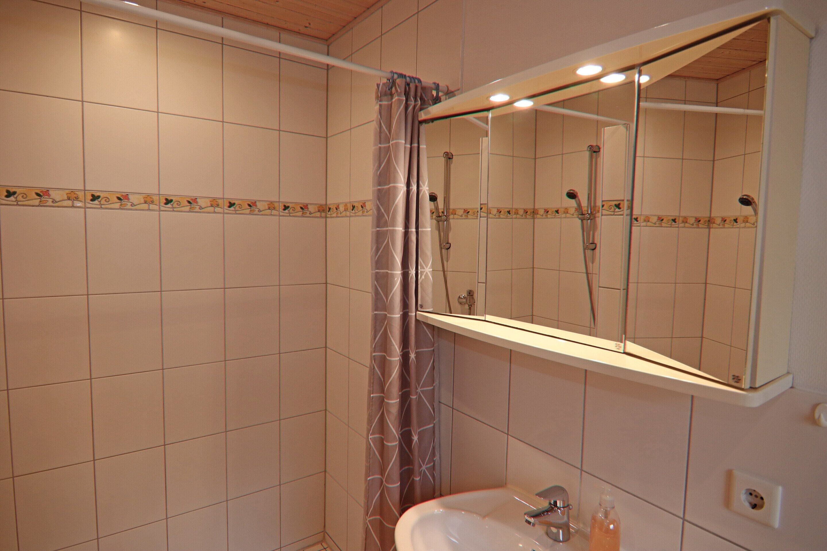 Un baño con ducha, lavamanos y espejo.