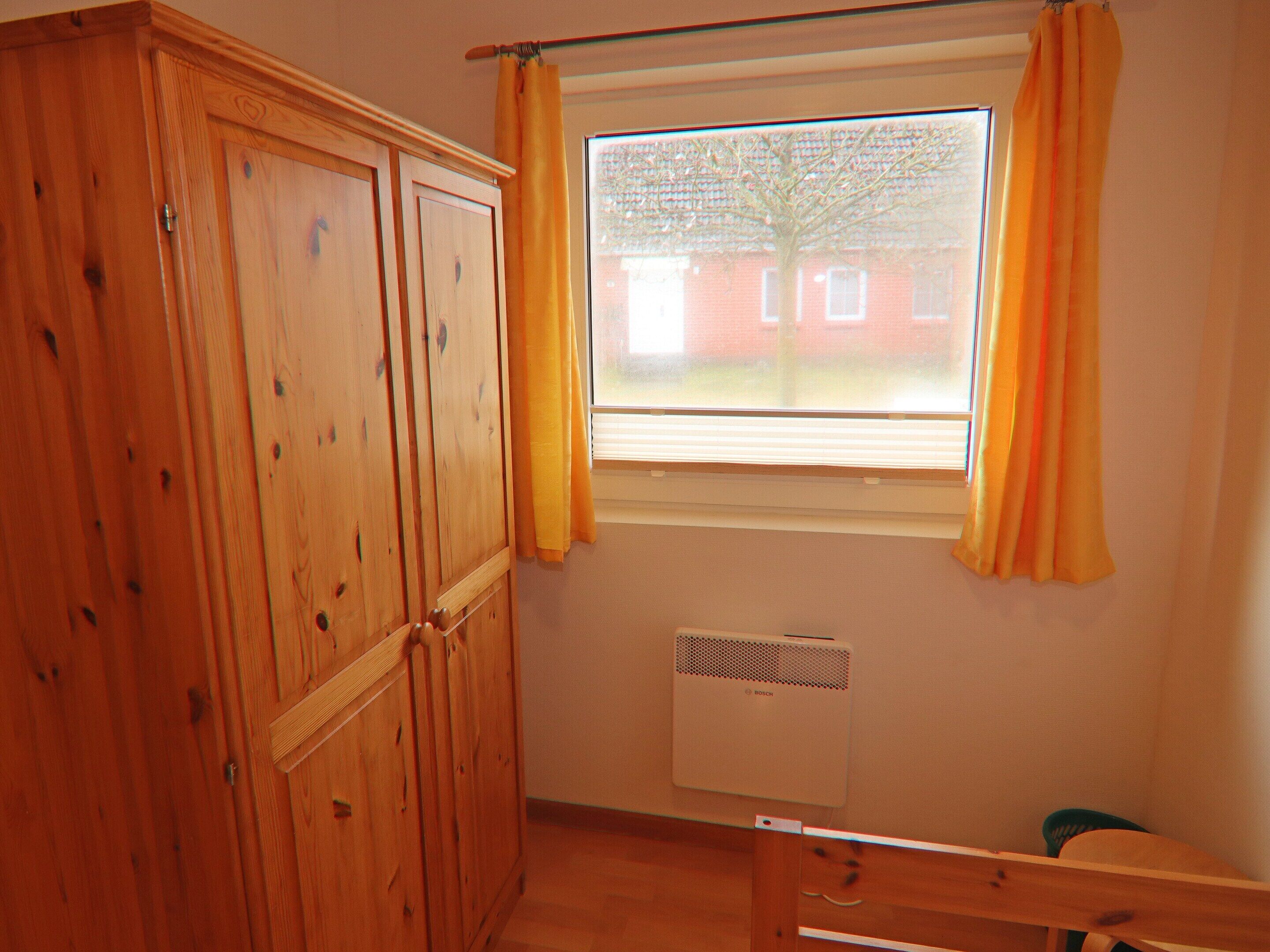 A room with a wooden wardrobe, a window with yellow curtains, and a radiator.