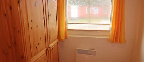 Une pièce avec une armoire en bois, une fenêtre ornée de rideaux jaunes et un radiateur.