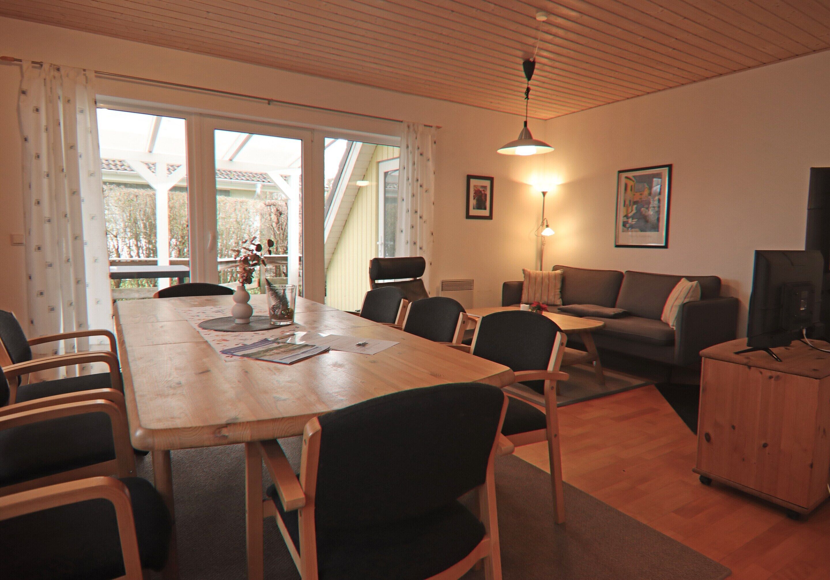 A spacious living area with a wooden dining table, multiple chairs, a sofa, and a television.