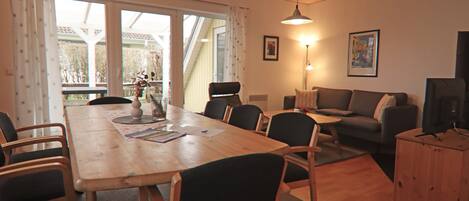 A spacious living area with a wooden dining table, multiple chairs, a sofa, and a television.