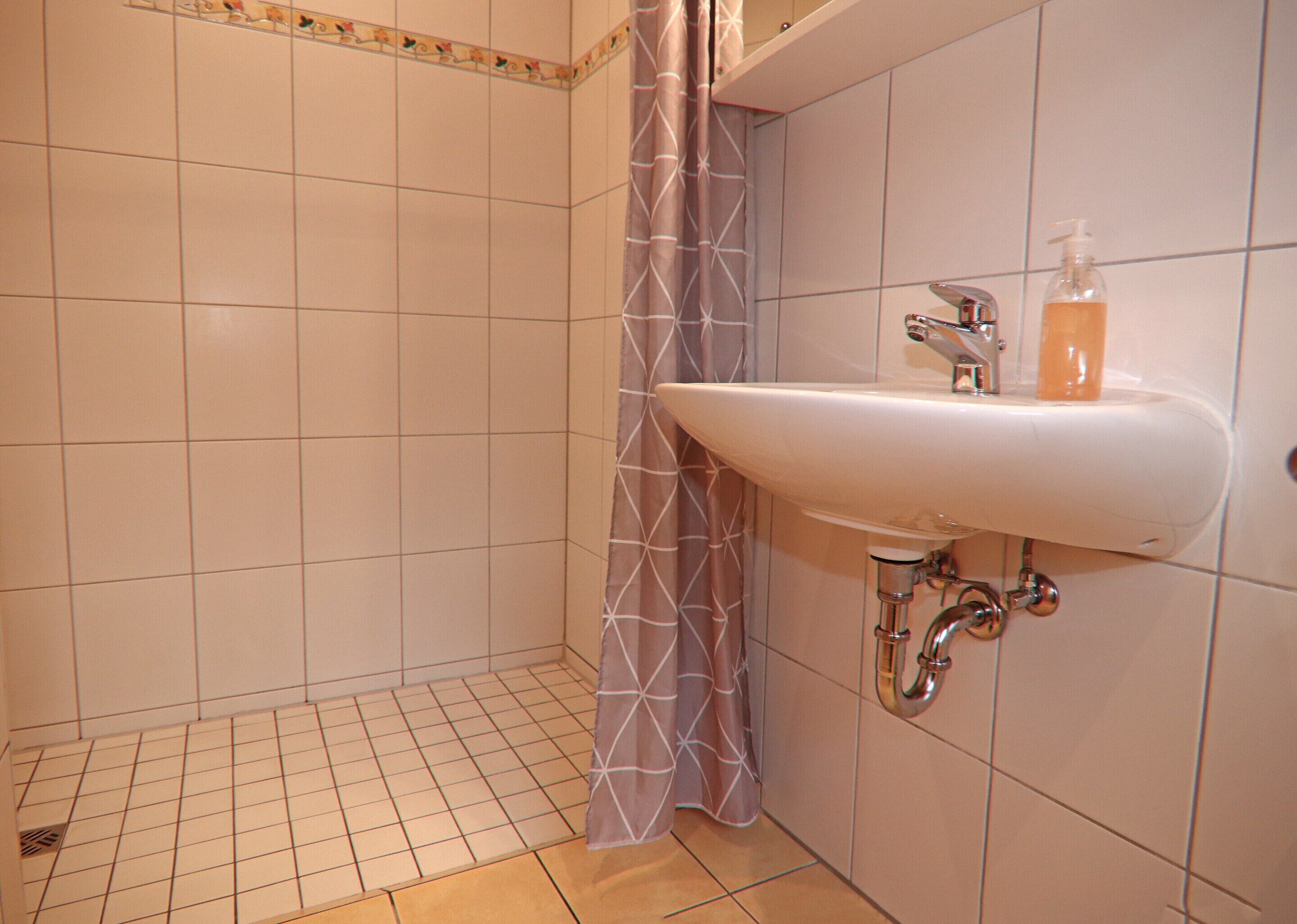 Une salle de bain avec un lavabo blanc, un rideau de douche et un sol carrelé.