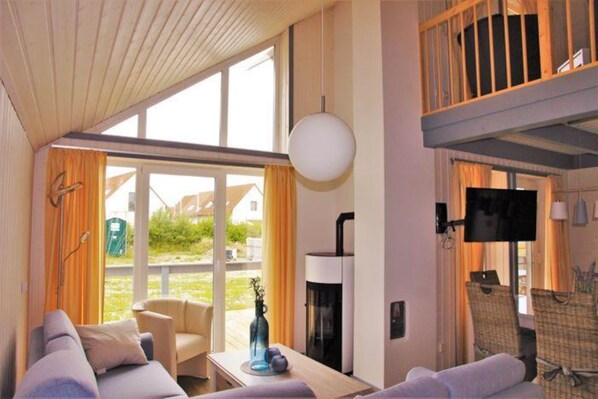 Ein modernes Hotelzimmer mit großem Fenster, einer Couch, einem Tisch mit Blumenvase, einem Flachbildfernseher und einem Kamin.