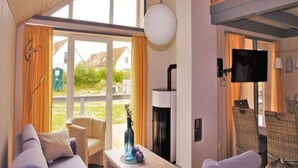 A hotel room with a large window, a sofa, a table with a vase, a flat-screen TV, and a fireplace.