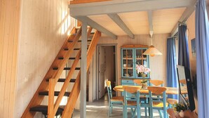 A wooden interior with a staircase, a dining area with blue chairs and a table, and a blue cabinet. - Exklusives Skandinavisches Ferienhaus (Mirow)