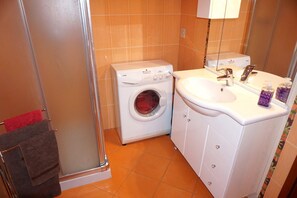 A compact bathroom with a washing machine, a sink, and a glass shower enclosure. - Apartment in Porto Santa Margherita (Caorle)