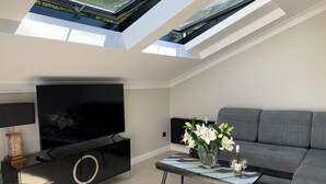 A modern living room with a flat-screen TV, a sofa, a coffee table with flowers, and a black entertainment unit. - Holiday Home in Miedzyzdroje for 8 Persons (Miedzyzdroje)