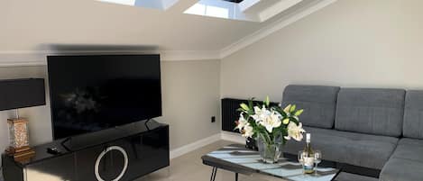 A modern living room with a flat-screen TV, a sofa, a coffee table with flowers, and a black entertainment unit.