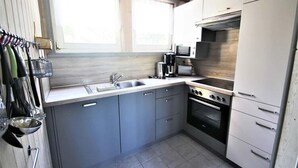 Une cuisine de taille réduite avec des meubles gris, une cuisinière en acier inoxydable, un four à micro-ondes et un évier.
