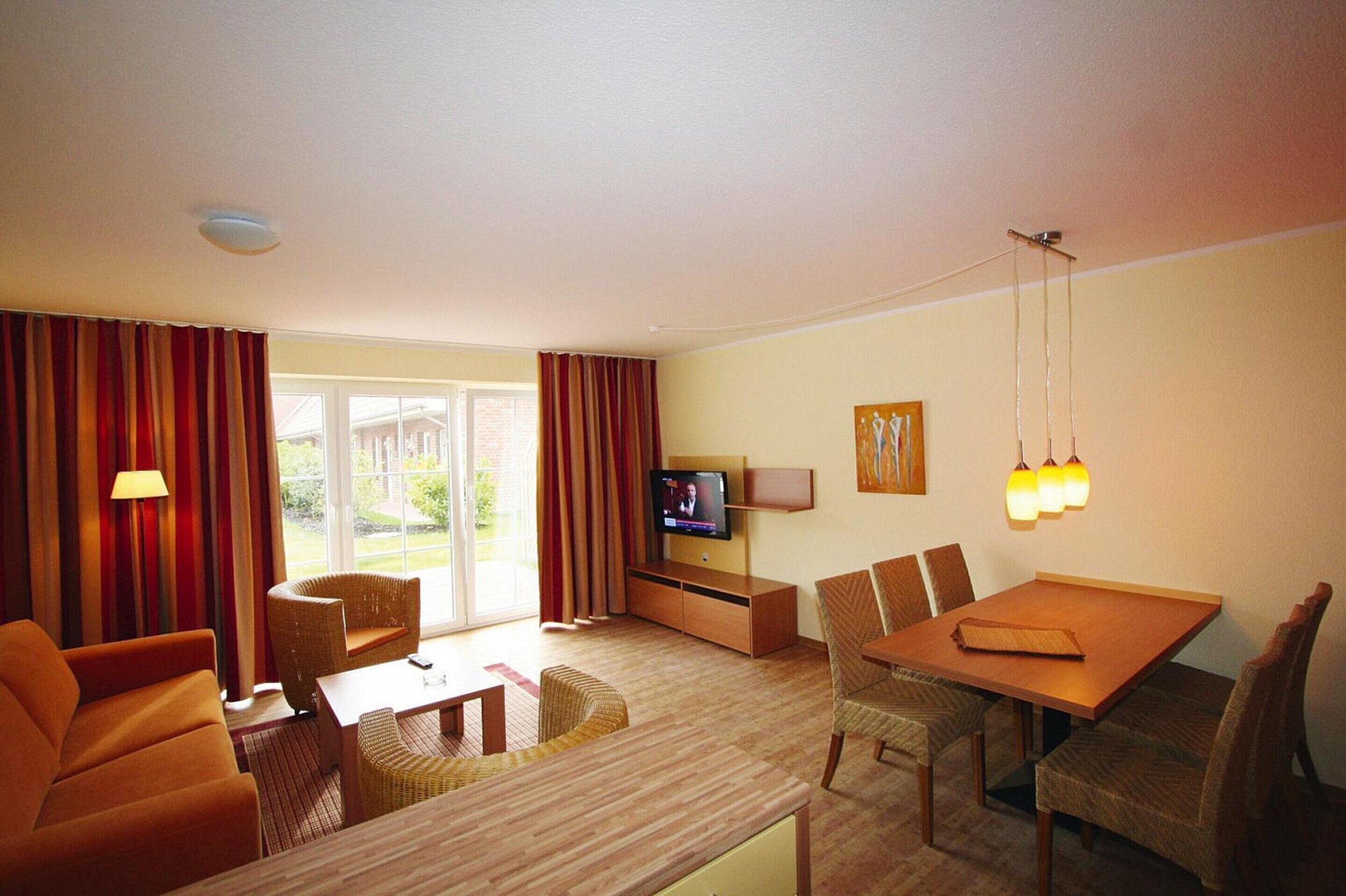 Une chambre d’hôtel avec un canapé, une table à manger et des chaises, un téléviseur posé sur un meuble, une lampe et une vue sur l’extérieur.