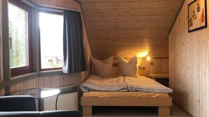 A cozy, wooden-paneled room with a bed, a small table, and a window with curtains. - Ferienhaus im Skandinavischen Stil (Mirow)