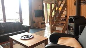 A cozy living room with a sofa, a coffee table, a fireplace, and a wooden staircase. - Ferienhaus im Skandinavischen Stil (Mirow)
