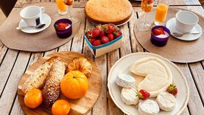 Une table en bois, dressée pour le petit-déjeuner, avec des croissants, des tranches d’orange, des fraises, du fromage et un gâteau.