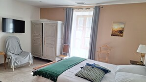 Une chambre à coucher comprenant un lit, une chaise, une armoire, un téléviseur et une fenêtre avec des rideaux.