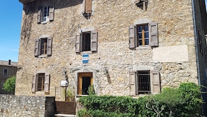 Un bâtiment en pierre avec un toit recouvert de tuiles, de nombreuses fenêtres dotées de volets et une enseigne.