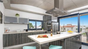 A modern kitchen with a central island, stainless steel appliances, and a view of the city through large windows. - Villa Primasol by Villa Plus (Punta Prima)
