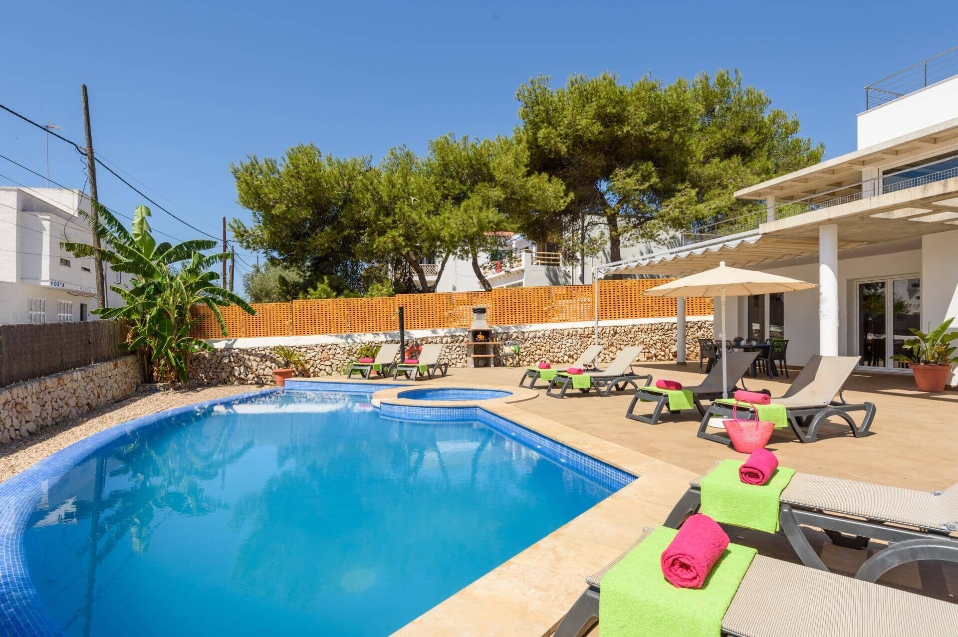 Une piscine entourée d’un mur de pierre et d’arbres, avec des chaises longues et des parasols à proximité.