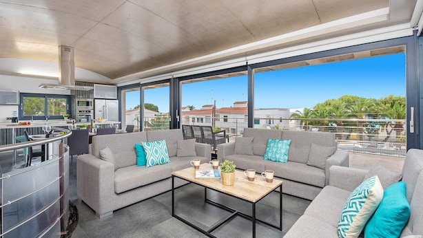 A modern living area with a sofa set, a coffee table, and a kitchen area visible through large windows. - Villa Primasol by Villa Plus (Punta Prima)