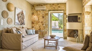 A cozy living room with a stone wall, a sofa, a coffee table, and a TV mounted on the wall. - Villa Kalou Cottage by Villa Plus (Ionian Islands)