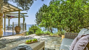 A stone patio with wicker furniture, a pergola, and a view of the sea. - Villa Kalou Cottage by Villa Plus (Ionian Islands)