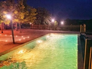 A rectangular pool with a gradient of green and yellow hues, surrounded by a wooden fence and trees.
