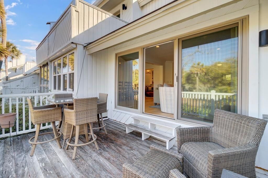 A wooden deck with wicker furniture and a sliding glass door leading to a room.