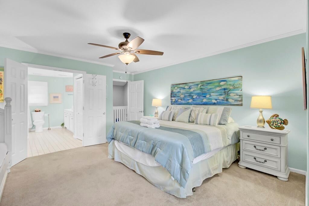 A bedroom with a bed, bedside tables, a ceiling fan, and a painting on the wall.