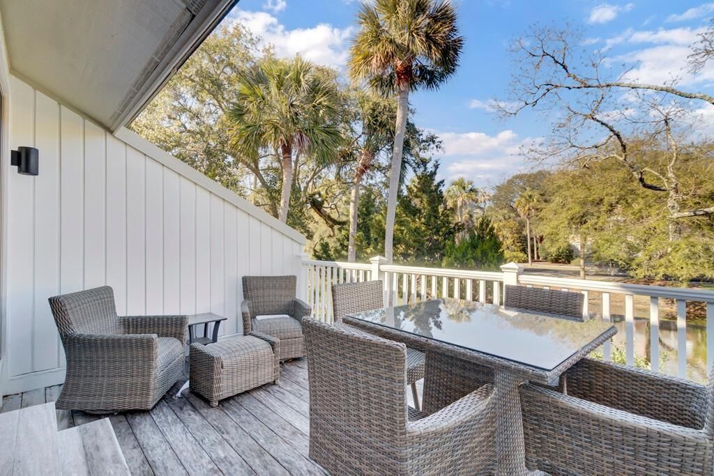 A covered outdoor deck with wicker furniture and a glass table, overlooking a body of water and trees.