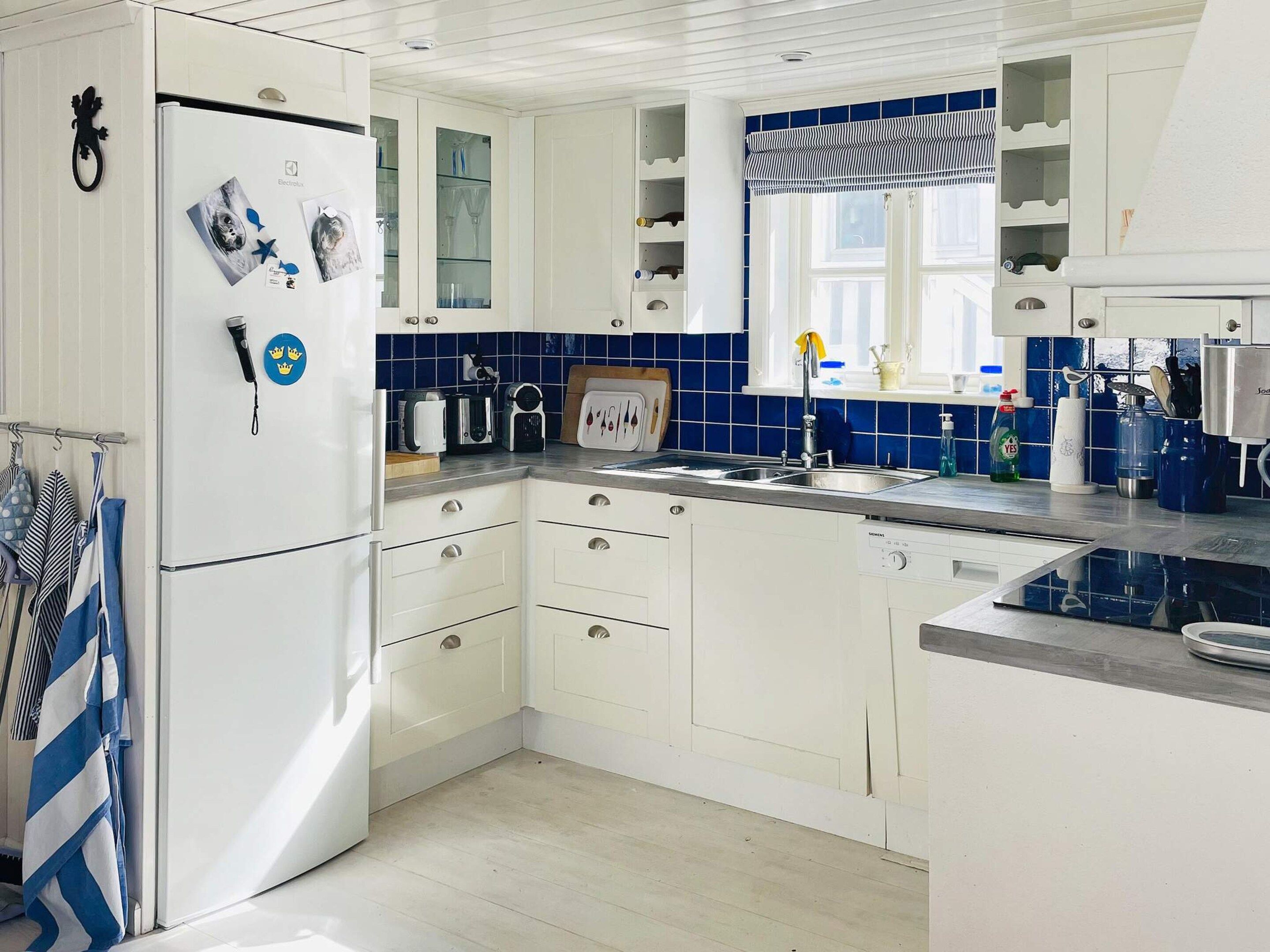 A kitchen with white cabinets, a built-in oven, a sink, and a window with a striped valance.