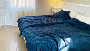 Et soveværelse med seng, natbord, lampe, et vindue med gardiner og en hvid stige op ad væggen.