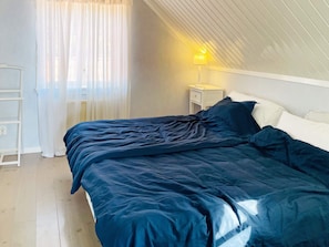 Un dormitorio con una cama, una mesita de noche, una lámpara, una ventana con cortinas y una escalera blanca adosada a la pared.