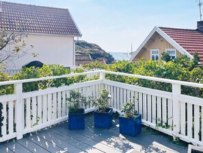 A wooden deck with a white railing, surrounded by greenery and houses with red-tiled roofs.