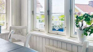 Et værelse med et bord og stole, store vinduer med hvide rammer, og udsigt til et hvidt hegn og grønt udenfor.