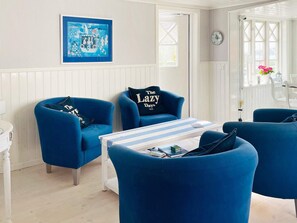 A room with a white paneled wall, a framed artwork, a table with striped tablecloth, and blue armchairs with pillows. - 4 Star Holiday Home in Kyrkesund (Kyrkesund)