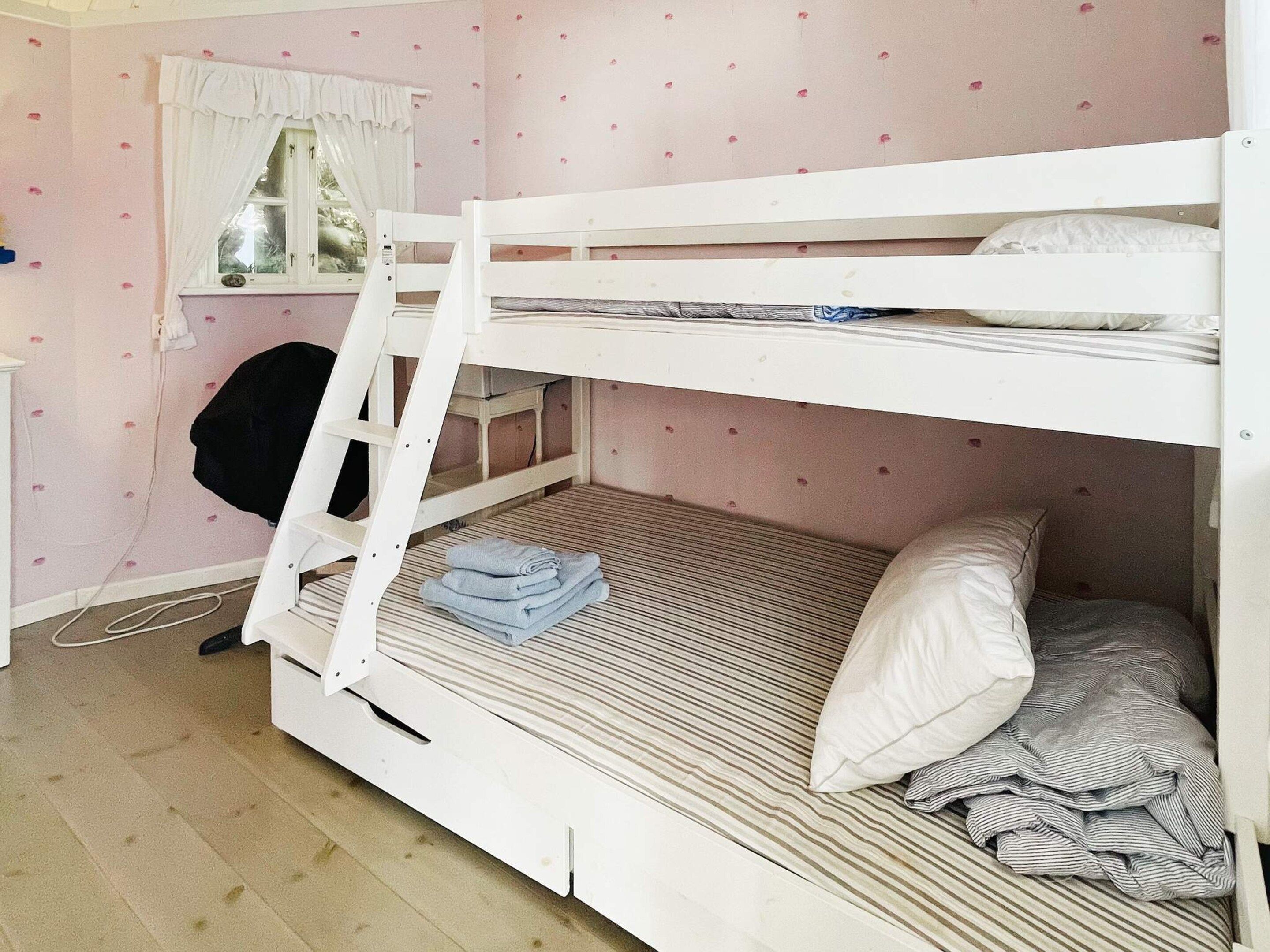 A bunk bed with a ladder, a window with curtains, and a desk with a chair.