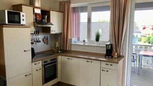 A compact kitchen with a microwave, stove, and sink. It features a sliding glass door leading to an outdoor area with a view of a balcony and a building. - Appartement im Ferienpark in Rechlin (Rechlin)