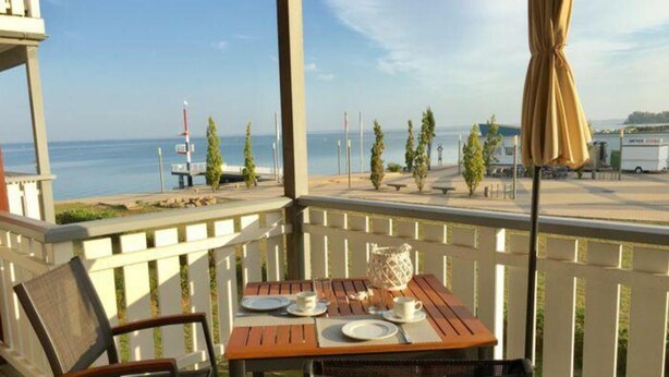 A wooden deck with a table set for two, overlooking a marina with boats and a clear view of the water. - Appartement im Ferienpark in Rechlin (Rechlin)