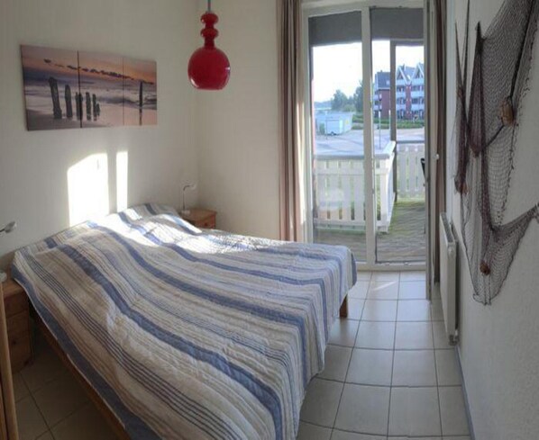 Une chambre avec un lit, une lampe suspendue rouge, un tableau au mur et une vue à travers une porte coulissante.