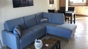 A modern living room with a blue sofa, a coffee table, and a painting of a sunset over water. - Appartement im Ferienpark in Rechlin (Rechlin)