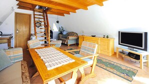 Una sala de estar acogedora con una mesa de madera, sillas, un televisor y una escalera que sube a una zona superior.