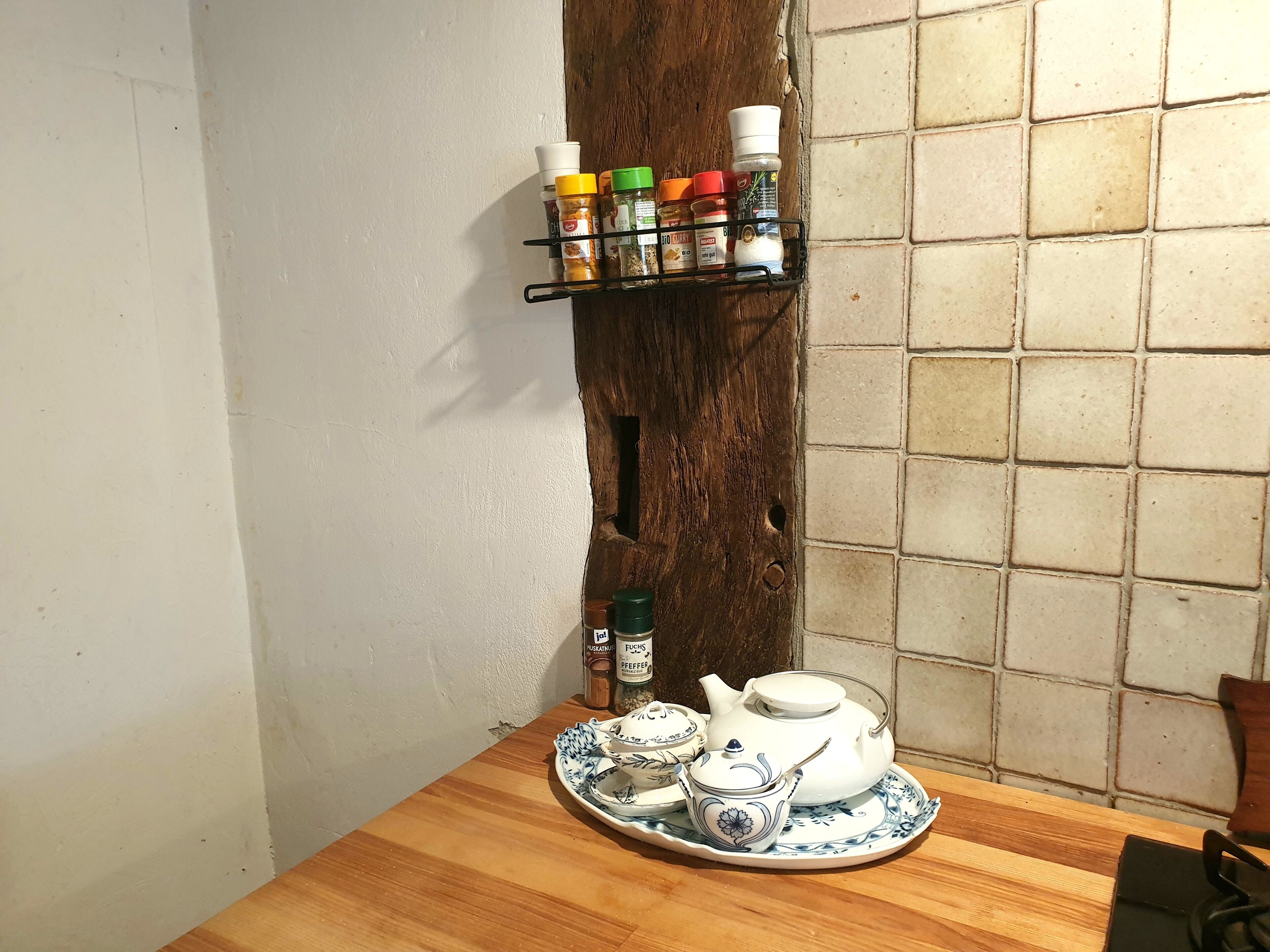 A wooden table with a tea set and spice rack against a wall with a wooden texture.