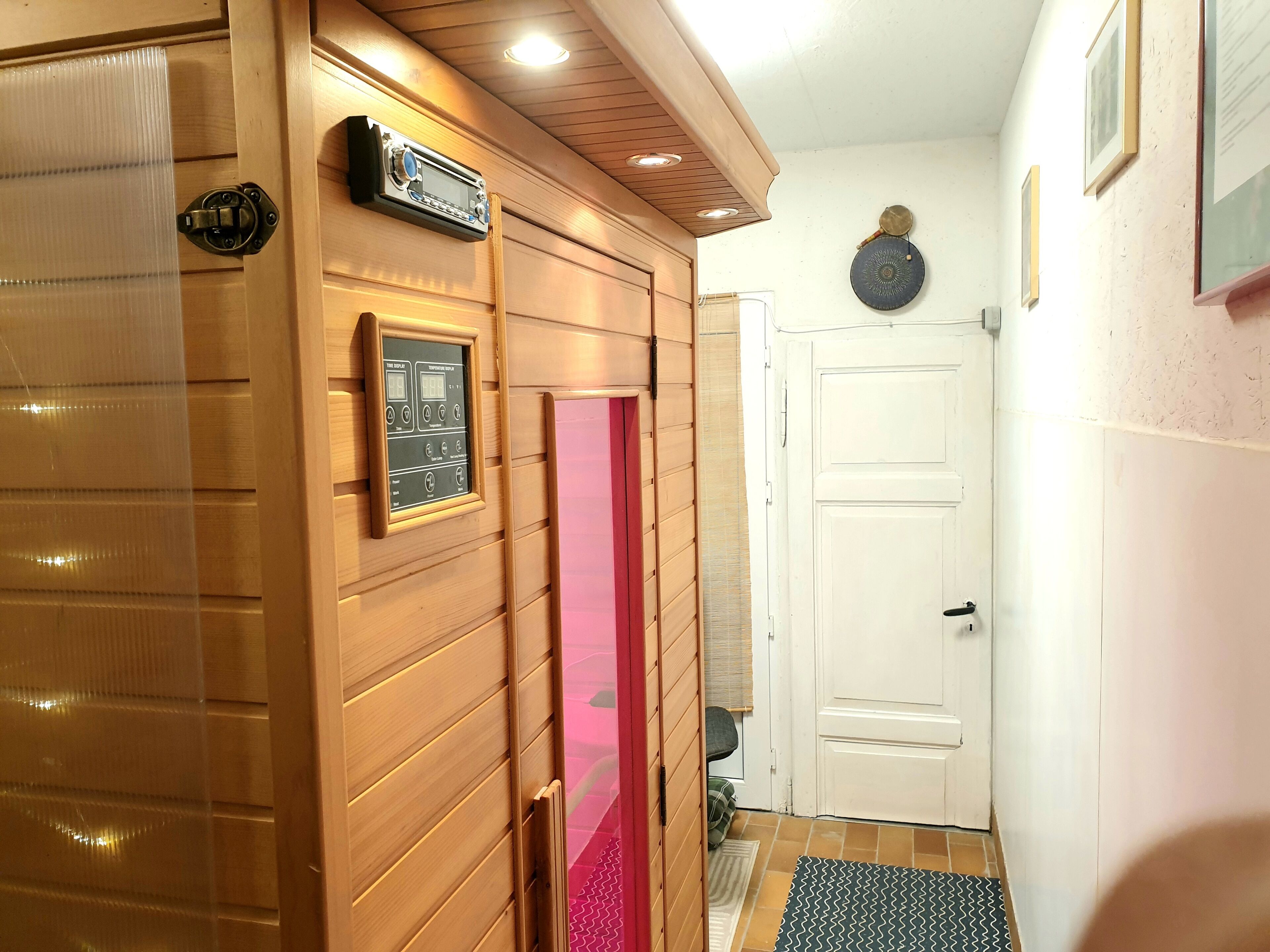En hall med träpanel på väggarna, en dörr med röd insida, en radio som hänger på väggen och en mönstrad matta.