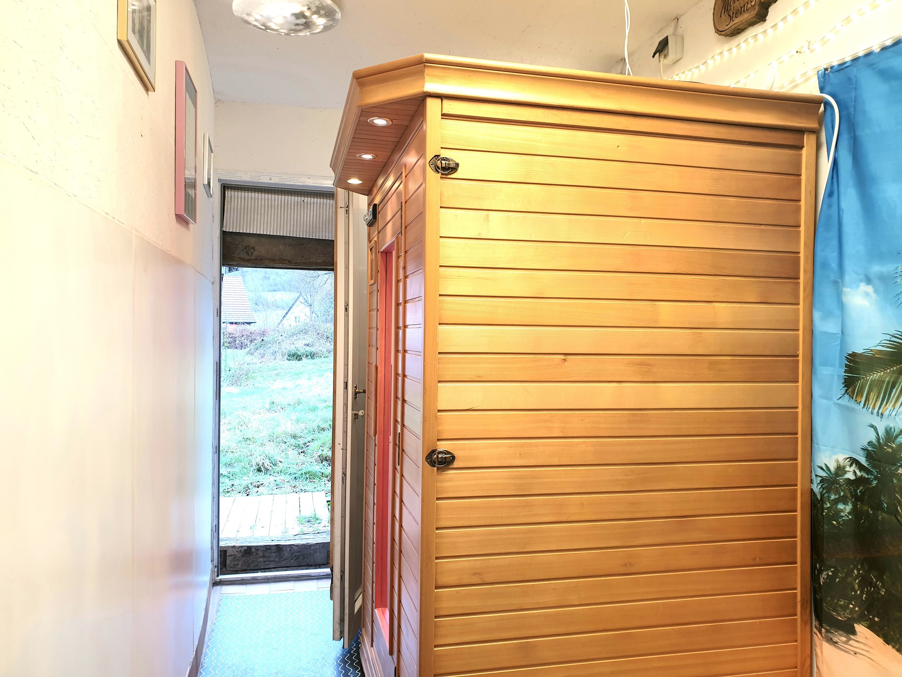 Un pasillo con una puerta de madera, vistas al exterior y una lámpara fijada a la pared.