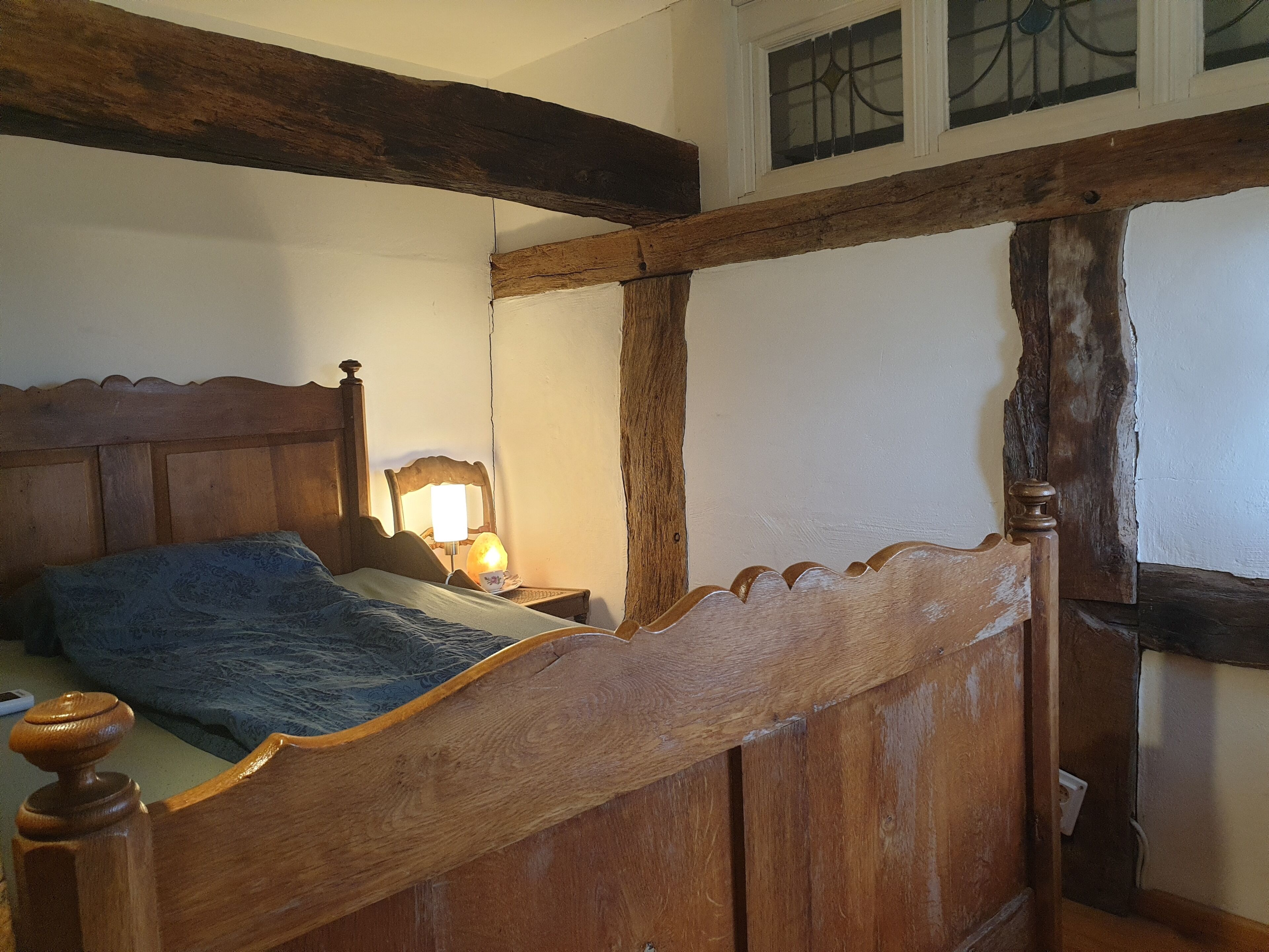 A wooden bed with a headboard, a bedside lamp, and a window with bars.