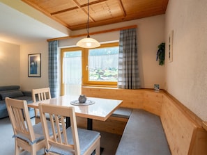 A cozy dining area with a wooden table and chairs, a bench, and a view of a village through large windows. - Magnificent Flat With Panoramic Views (Gaschurn)