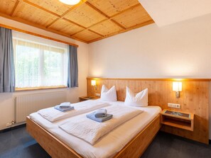 A hotel room with a large bed, wooden headboard, two bedside tables, and a window with curtains. - Magnificent Flat With Panoramic Views (Gaschurn)